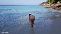 Une fille rousse nue se baigne sur une plage publique